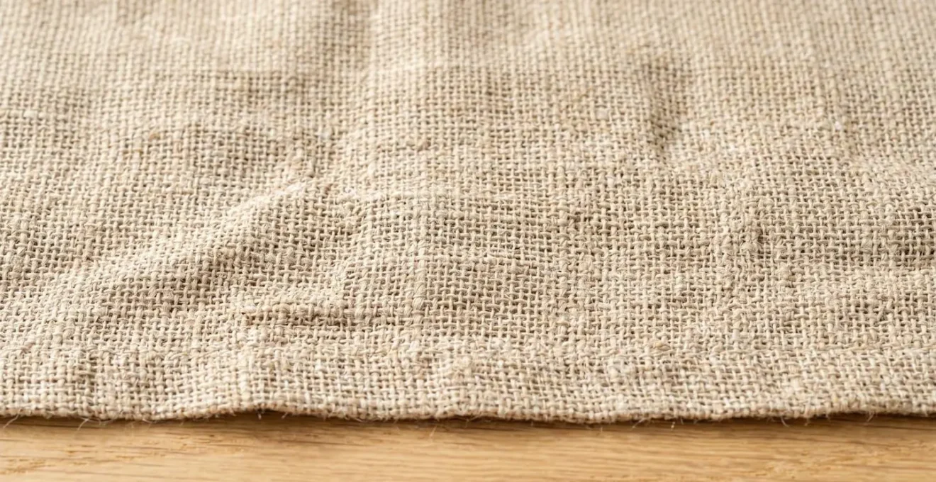Gros plan sur la texture d'un tissu en lin naturel beige clair montrant le tissage aéré et les plis naturels sous lumière rasante
